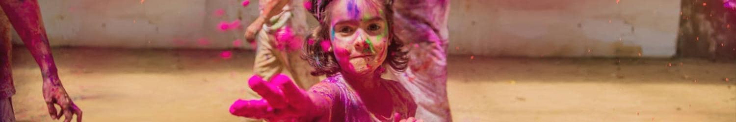 Holi kutlamaları sırasında yüzünde renkli pudra olan ve elini uzatan çocuk.