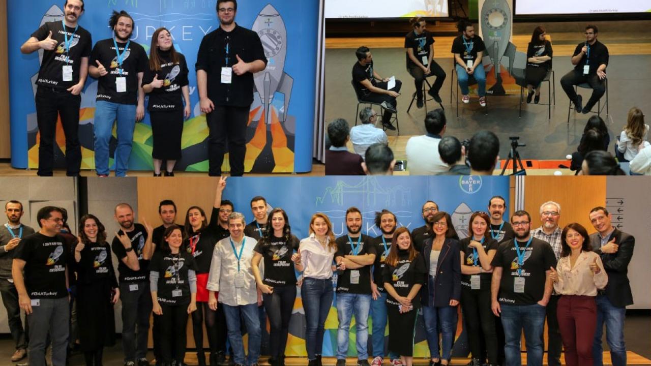 Uzay temalı grafiklerin yer aldığı pankartların önünde, markalı tişörtler giymiş bir teknoloji etkinliğinde poz veren insanlar.