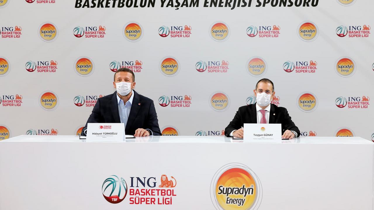 Takım elbiseli, maskeli iki adam, ING Basketbol Süper Ligi ve Supradyn Energy logolarının bulunduğu bir masada oturuyor. Bir sponsorluk etkinliğinde gibi görünüyorlar.