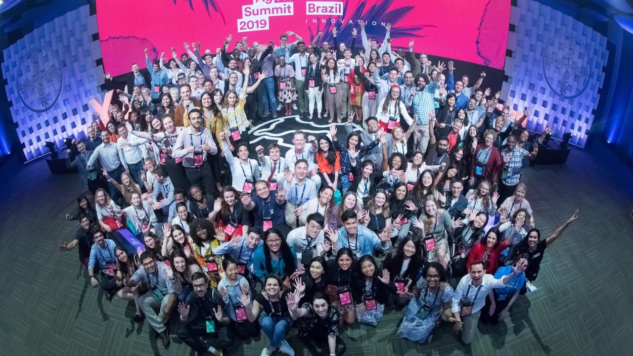 Brezilya'daki 2019 Gençlik Tarım Zirvesi'nde sahne arkası ve etkinlik tabelalarının görülebildiği büyük bir grup insan birlikte poz veriyor.