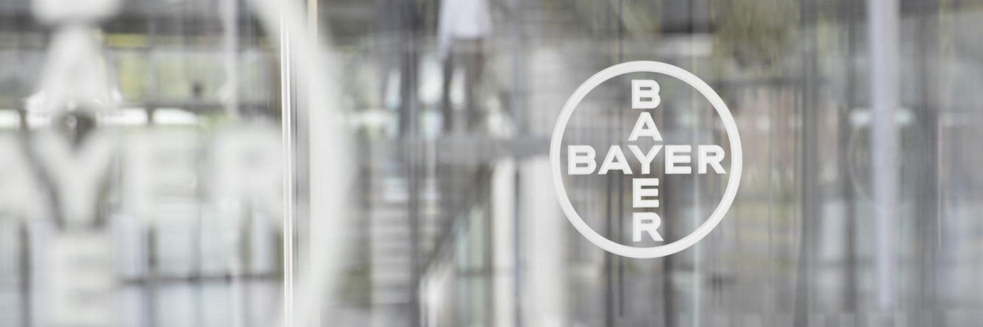 Bulanık arka planda insanları ve merdiveni gösteren cam pencere üzerindeki Bayer logosu.